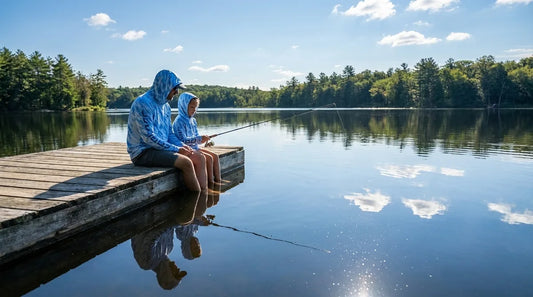 father and young daughter fishing from a wooden backyard dock on a calm lake, both wearing hooded sun shirts, bright midday sun, water reflections visible