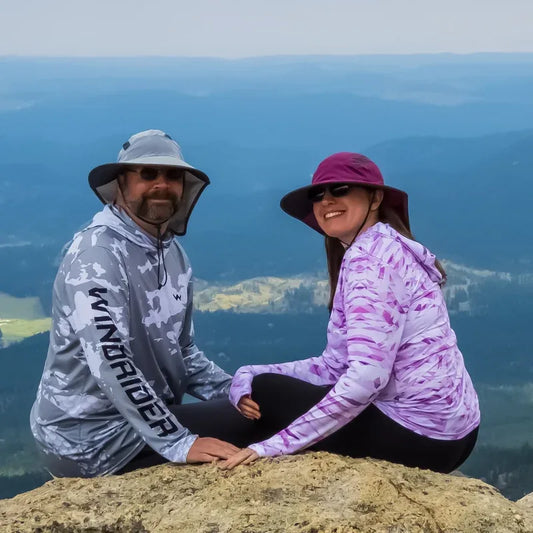 Couple wearing WindRider Helios sun shirts outdoors on mountain summit in bright sunlight