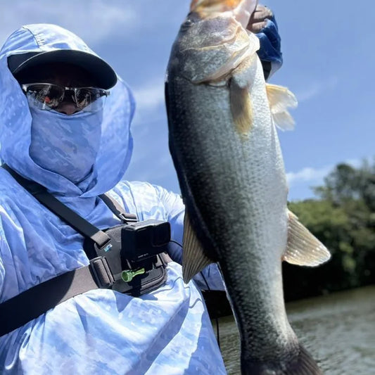Angler wearing full sun protection system — hooded Helios shirt with face gaiter, gloves, and sunglasses — while fishing on a sunny day