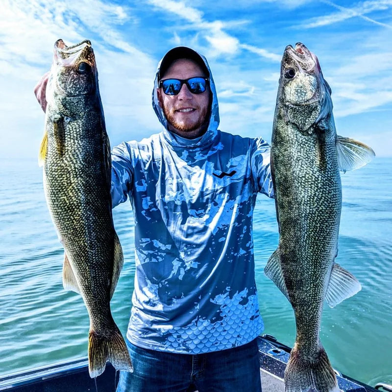 Angler wearing hooded Helios sun shirt on offshore boat holding walleye against turquoise water
