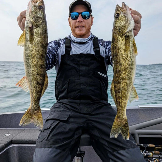 Angler wearing WindRider waterproof rain bibs holding two trophy walleye on boat in overcast conditions