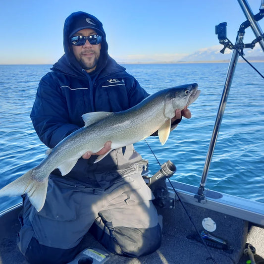 Angler in waterproof hooded rain jacket holding lake trout on boat in open water