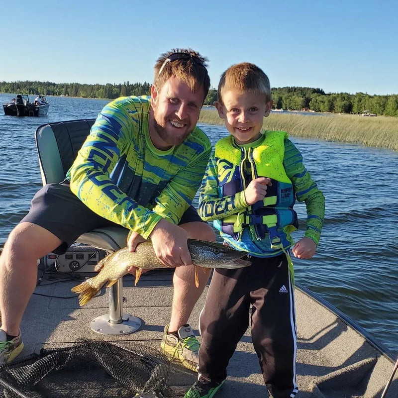 Father and son in matching Helios sun protection shirts holding pike on fishing boat