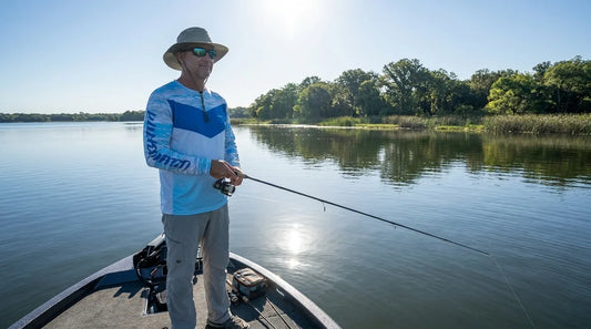 angler in their 50s standing on a flat-water boat in bright midday sun, wearing a light-colored long-sleeve UPF shirt, calm expression, visible sun glare on water
