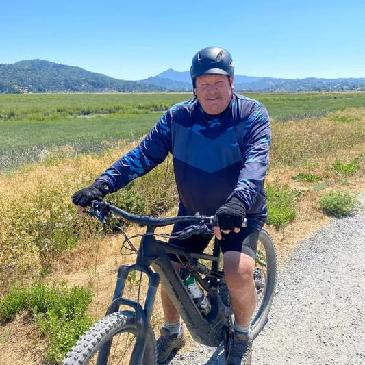 Man in Helios UPF sun shirt on outdoor trail with mountains and bright sky — athletic sun protection for running