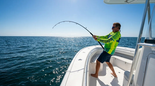offshore angler on the bow of a sport fishing boat, open blue water, midday sun directly overhead, wearing a long-sleeve UPF shirt while holding a bent rod with a fish on