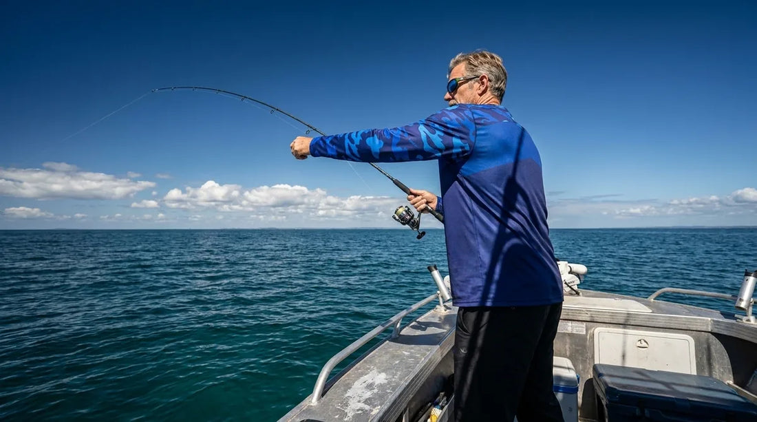large-framed angler in long sleeve fishing shirt standing on a boat deck, midday sun overhead, casting with full arm extension showing sleeve coverage to the wrist