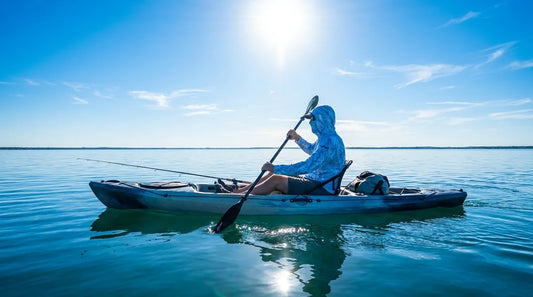angler in hooded sun shirt paddling a kayak on calm water, bright midday sun overhead, fishing rod secured to side, water reflecting light