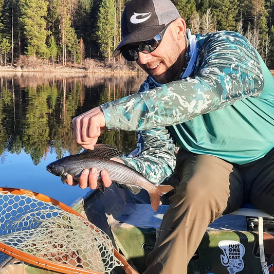 Angler wearing sun protection shirt while kayak fishing on a calm mountain lake