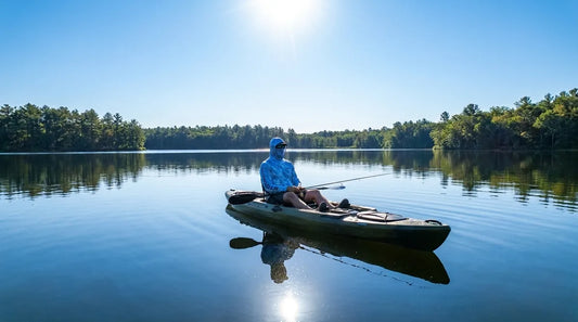 kayak angler paddling on calm lake at midday, bright overhead sun, wearing hooded long-sleeve sun shirt, fishing rod across lap, water reflecting intense light at face level