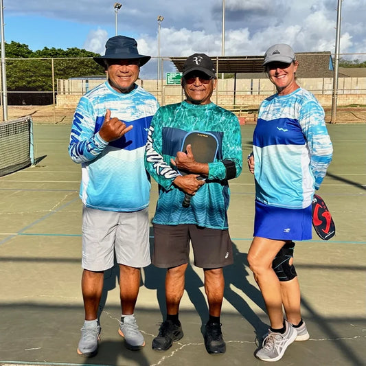 Friends wearing WindRider Helios UPF 50+ sun shirts on outdoor court in sunny conditions