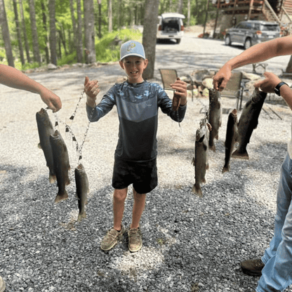 Young boy in blue grey HELIOS sun shirt displaying caught fish with family outdoors